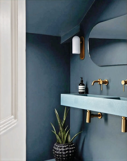 Contemporary bathroom with deep blue plaster walls, a floating rectangular sink, a round mirror, and a brass wall-mounted faucet. A modern white sconce and a striped soap dispenser add stylish accents to the minimalist design.