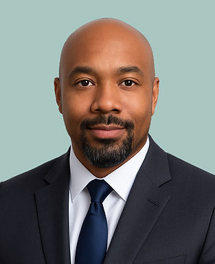 Professional headshot of a man in a dark suit and navy tie, with a trimmed beard and shaved head, posed against a light blue