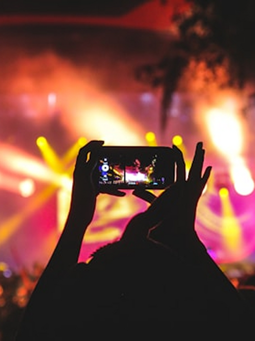 Person holding phone recording concert with bright lights and smoke.