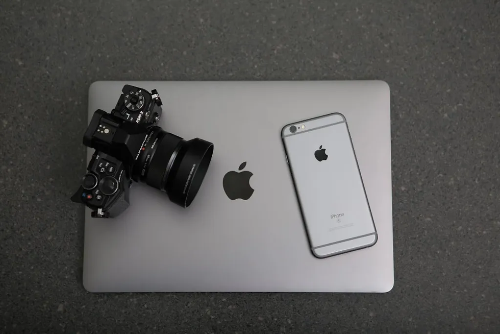 Camera and iPhone resting on a silver MacBook with Apple logo. Gray textured surface background. Simple, tech-centric composition.