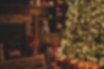 Lit Christmas tree with ornaments beside a stone fireplace. Gifts wrapped in red ribbons are on the floor, creating a cozy holiday mood.