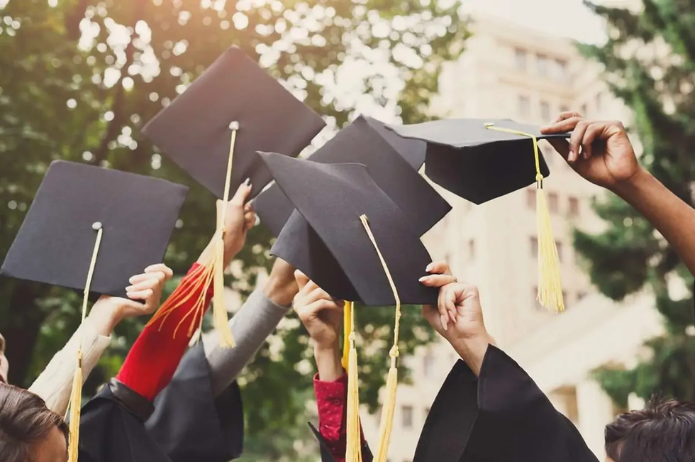 Graduates celebrate by raising caps in the air outdoors, with sunlight filtering through trees. The mood is joyous and triumphant.