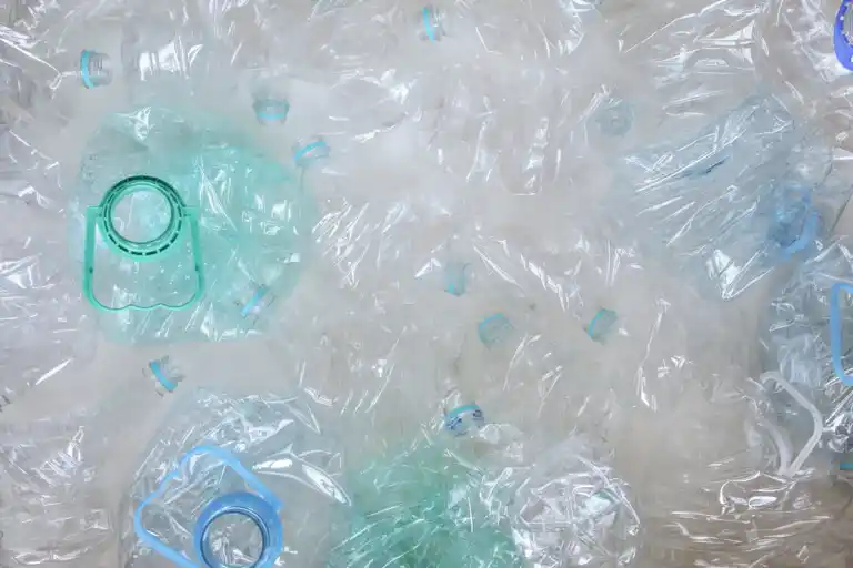 Crushed plastic bottles with blue and green caps scattered against a light background, creating a chaotic and cluttered impression.