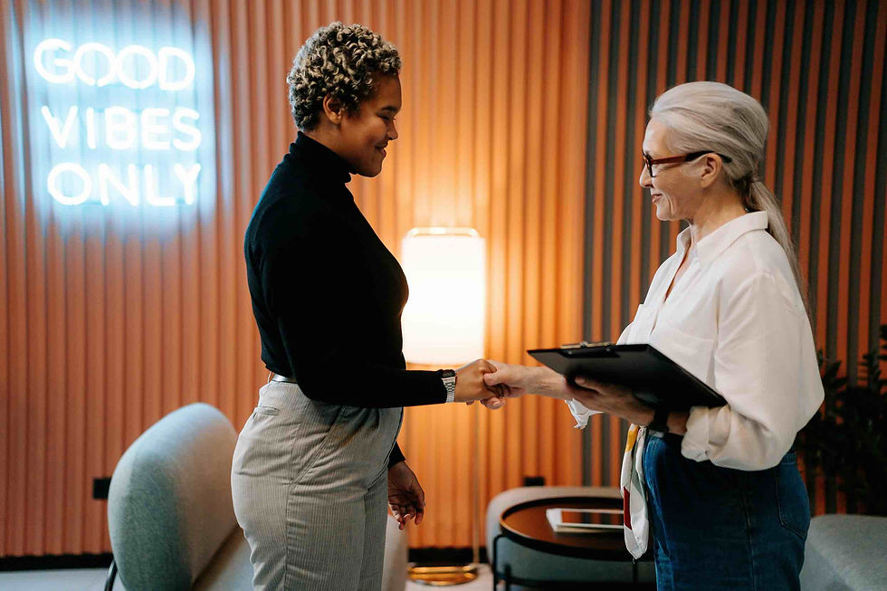 Two people shake hands, smiling in a room with a neon sign reading "GOOD VIBES ONLY." Warm lighting and modern decor create a positive mood.