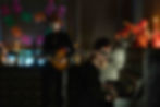 Two people with face paint in a dim room; one plays piano, the other guitar. Bright candles, flowers, and colorful banners decorate the space.