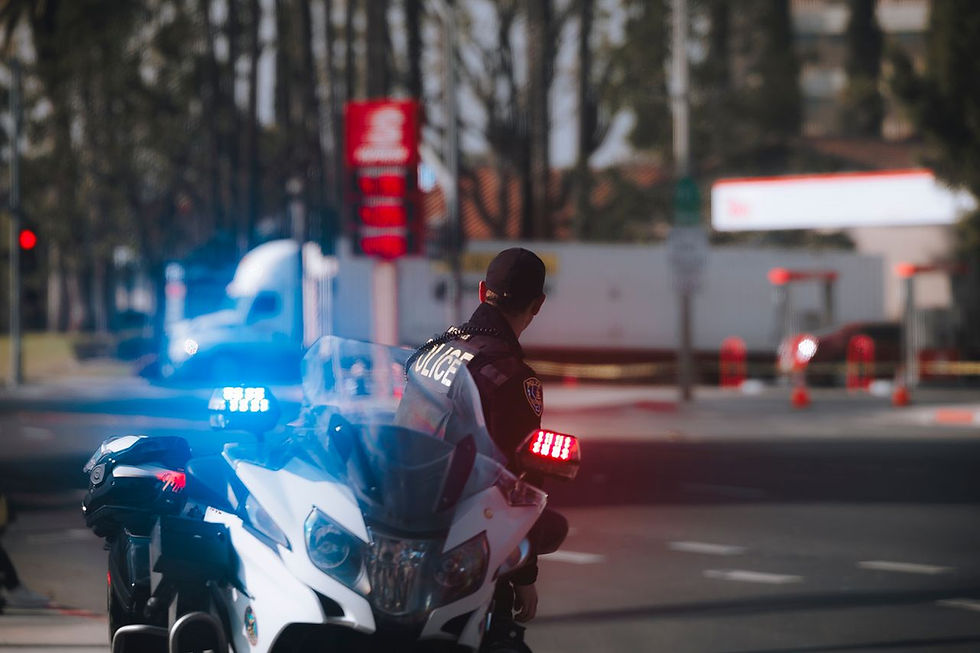 Police officer on motorcycle with flashing lights on city street during daytime.