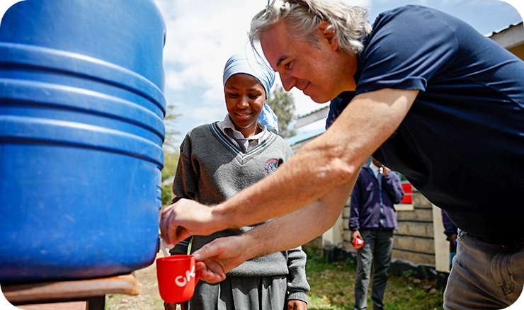 Während des Projektbesuchs: Olaf Bachert und eine Schülerin beim Wasserzapfen aus einem 'blue tank' des Safe Water-Programms an der Ilmashariani Secondary School in Nairobi.