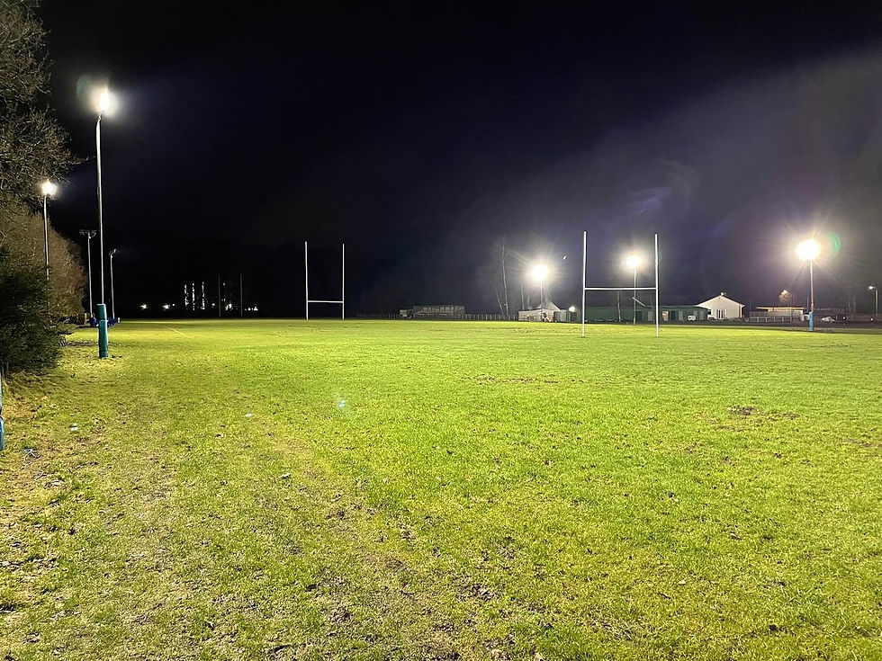 Eye-level view of an upgraded rugby pitch with bright floodlights shining at night