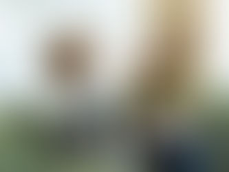 Man and woman high-five on green sofa. Man holds laptop; both smiling. Bright room with curtains; casual, happy mood.