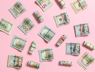Rolled and stacked US dollar bills secured with rubber bands on a pink background, featuring various denominations including 100 and 5.