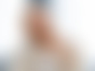 Man with glasses and a beard, thoughtfully touching chin, wearing a striped shirt. Bright, blurred interior background, conveying curiosity.