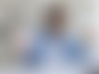 Smiling man holds pink piggy bank and fan of cash in office with white shelves. Wears blue shirt and glasses, expressing happiness.