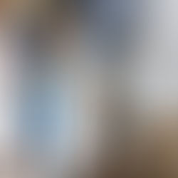 Two people in gloves cut wood on a sawhorse using a red saw. Paint-splattered jeans; paint cans and a brush visible on the floor.