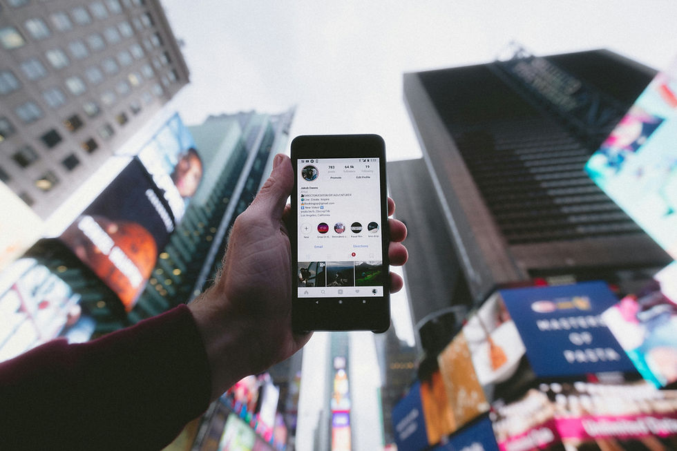 Cell phone held in the sky between brightly lit billboards on skyscraper buildings.
