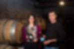 Two wine makers in a cellar holding bottles of wine with barrels behind them - Local Things to Do in Barcelona