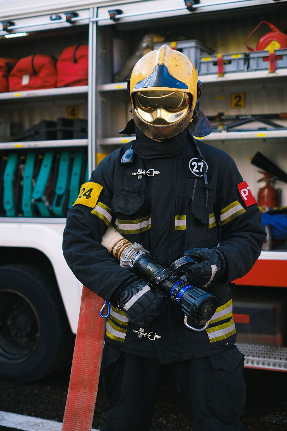 A firefighter in full gear holding a hose in front of a fire truck