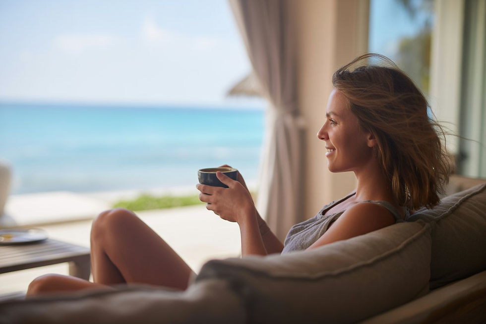 A woman smiles while holding a cup on a patio with an ocean view. Relaxed mood, soft lighting, and gentle sea breeze.