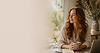 Woman with auburn hair sitting beside a window in a warm, light-filled workspace, representing friendly customer support for Inner Life School online personal development courses.