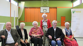 Senioren-Treffen in der Sporthalle: Sechs ältere Personen in Tracht und Anzügen posieren für ein Foto.