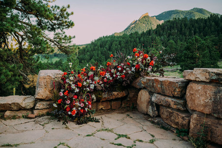 Elopement photoshoot on a mountain in Colorado with a large bold floral arrangement and the Colorado mountains in the background, where the two brides will hold their elopement ceremony.