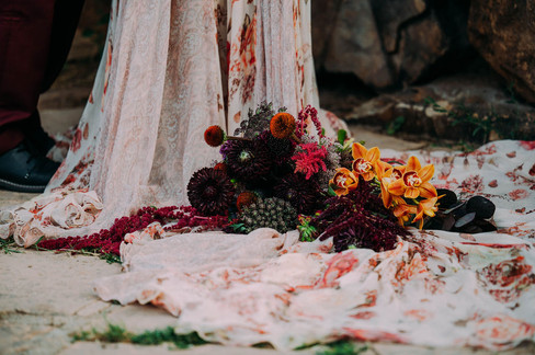 Bold fall floral arrangement for a Colorado elopement photoshoot with Alex Medvick, the bouquet is draped across the train of a floral maroon and white wedding dress and close up.