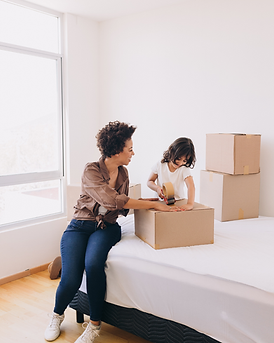 Mother packing moving boxes on a bed with her child while preparing for a new home.