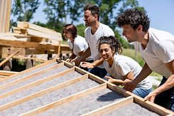 Group of people lifting a wall beam together, symbolizing building a home and support.
