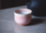 Front view of a modern, minimalist shaped ceramic cup with shiny, light pink glaze and white interior on grey marble.