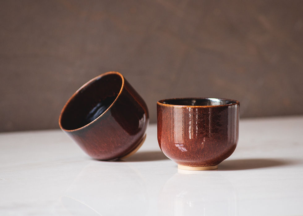 Thumbnail: Front view of two minimalist, round, handmade ceramic Cortado cups in brown glaze on a white marble surface. One on its' side