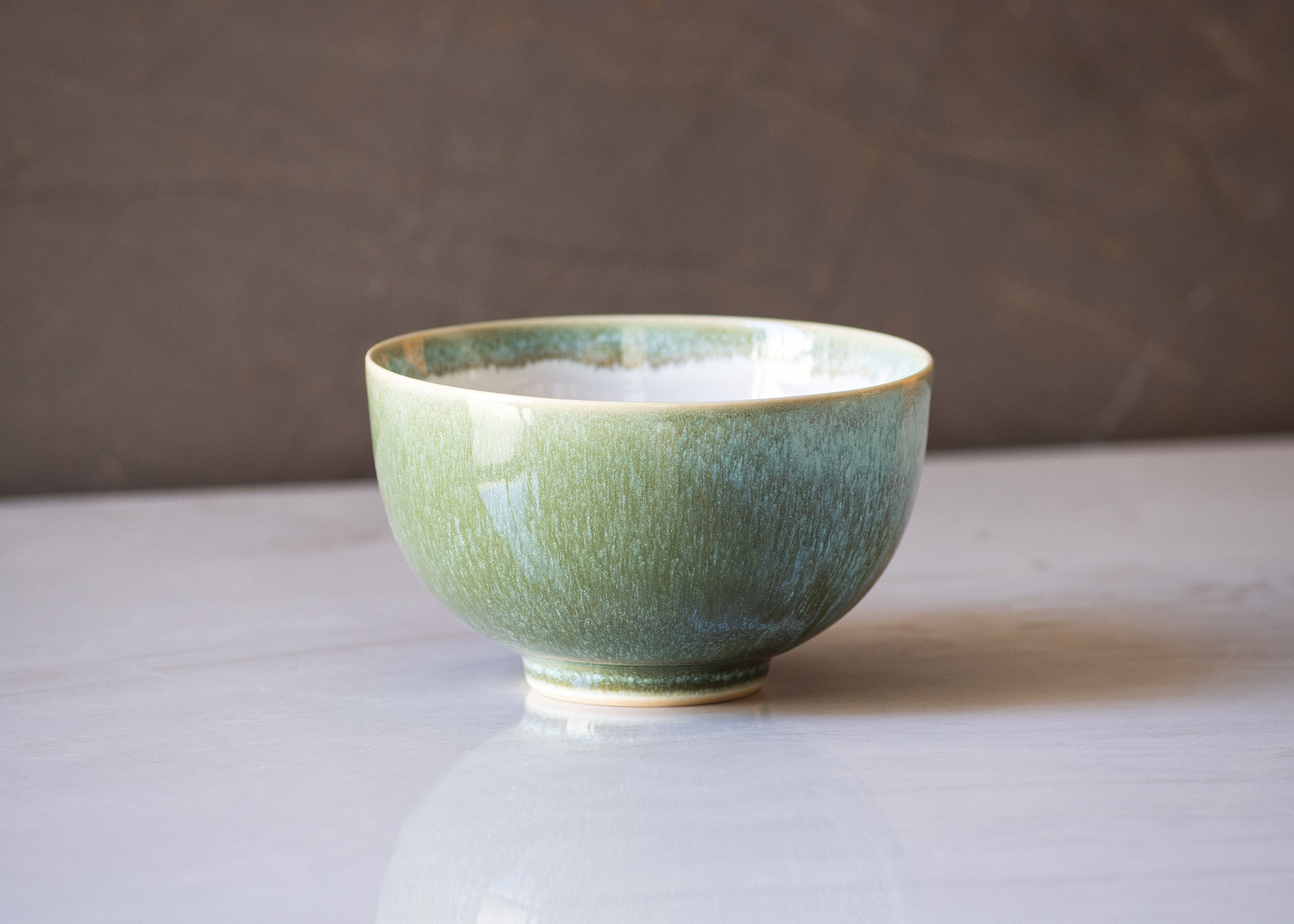 Front view of a minimalist, matcha tea ceremony bowl in green on a white marble surface with soft lighting.