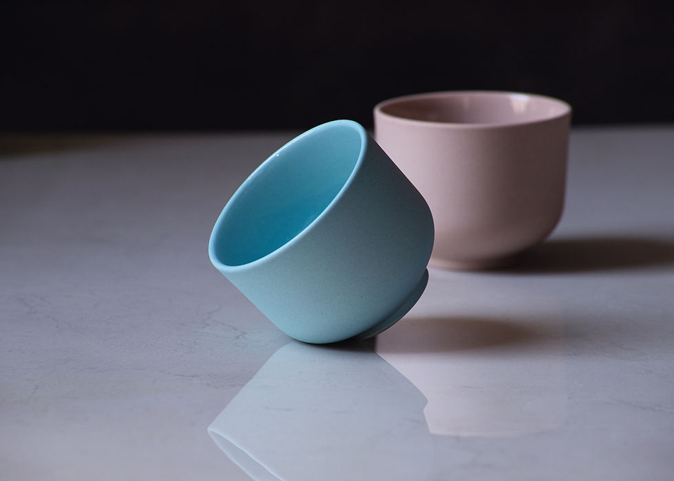 Thumbnail: Front view of two minimalist, modern, round espresso cups on a marble surface. One, on its' side, in blue and one in brown.