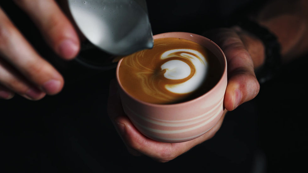 Thumbnail: High view of a minimalist, round, stoneware cup in pink with white swirls in which a barista is making latte art.