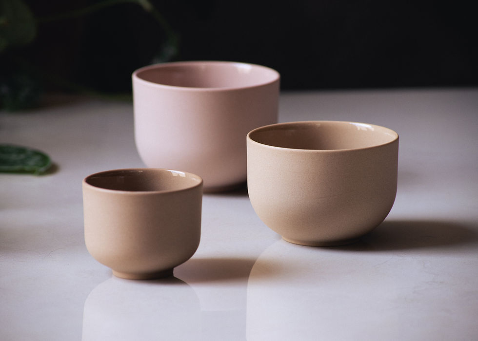 Front view of three round, minimalist, stoneware coffee cups in beige and pink on a grey marble surface.