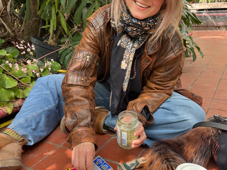 A girl sitting on stone ground in a greenhouse rolling a cigarette.