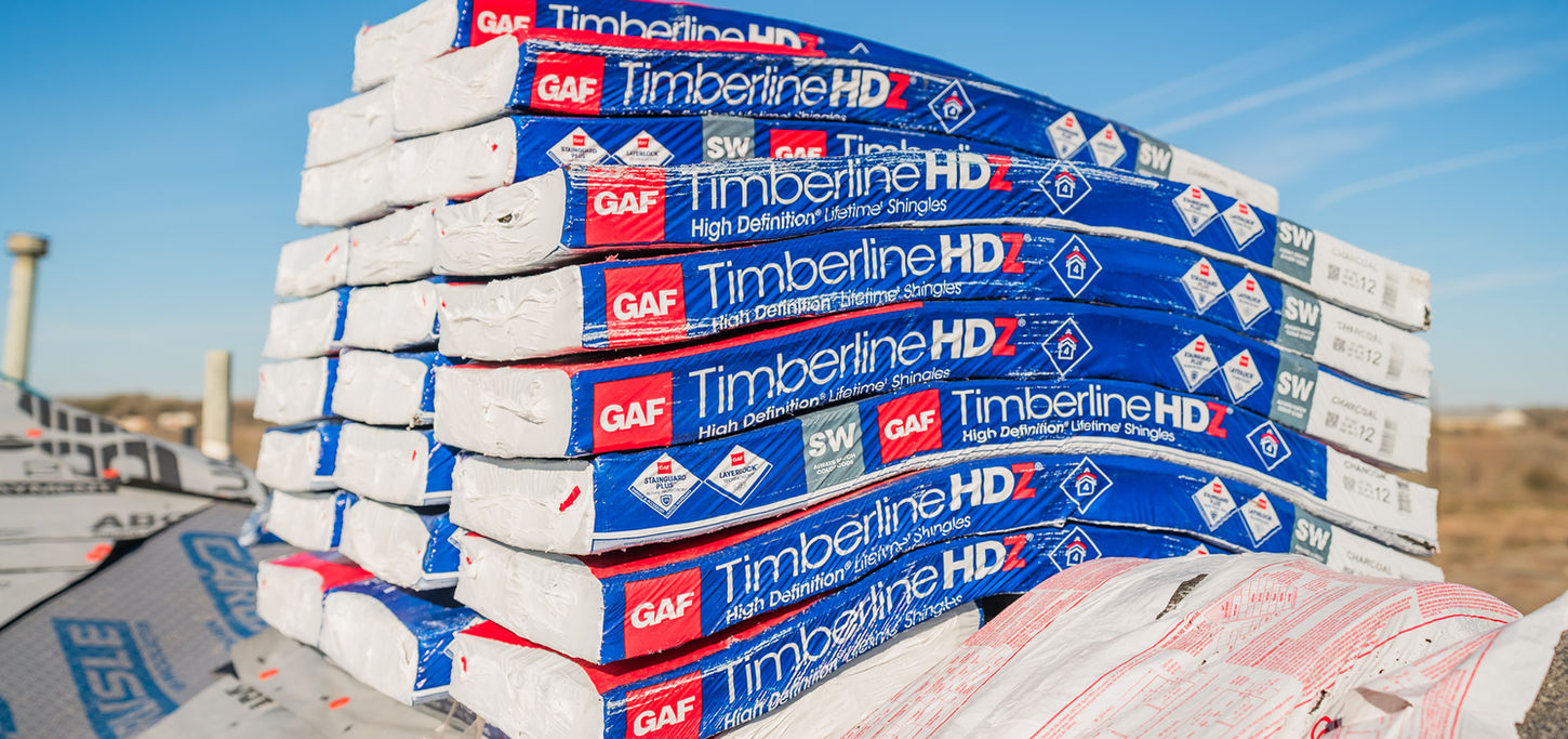 Bundles of GAF Timberline HDZ shingles stacked on a roof covered with synthetic underlayment, ready for installation.
