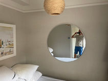 round mirror hanging on bedroom wall showing light shade and picture on other wall