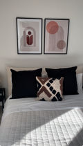 Two pictures hung on wall above bed with pillows and made up bed