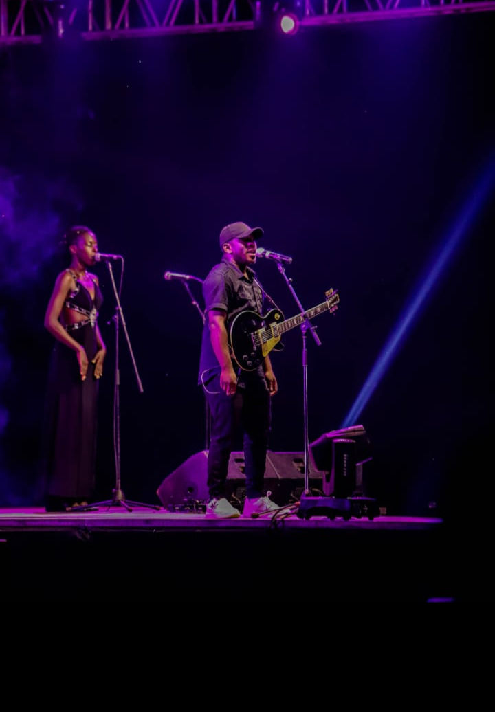 A man and a woman on a stage performing. She is singing and he is playing the guitar.