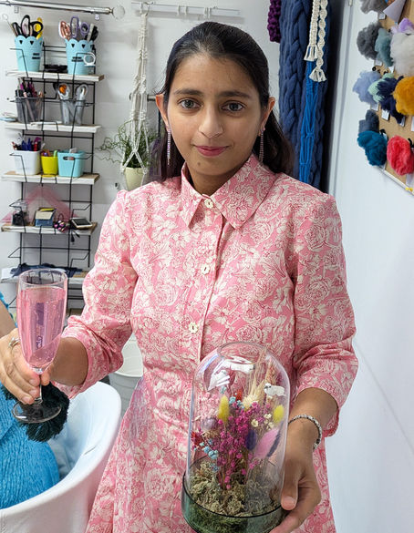 Customer sharing her sewing makes and sewing journey after learning to sew with Create and Sew Studio in Chorley. Sewing machines in the background, woman wearing dress she made herself and a floral arrangement made in a class with Create and Sew Studio