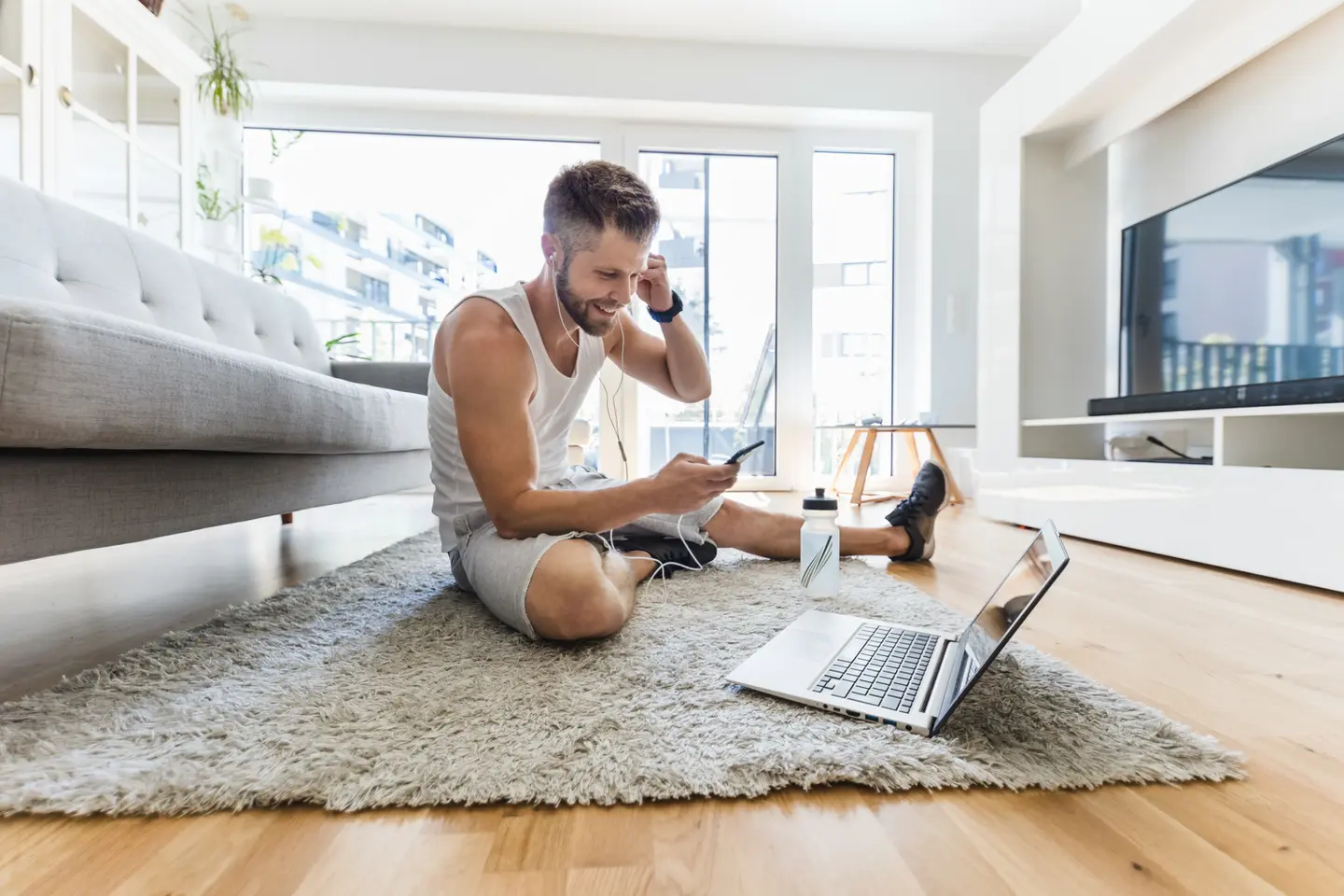 Man checking phone, laptop nearby, home workout