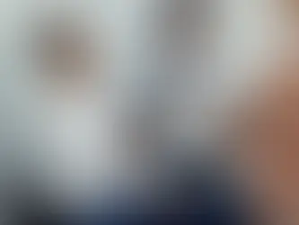 Man in a white shirt smiles, holding a tablet and handing a document to a woman. Another woman in a suit watches. Bright, indoor setting.