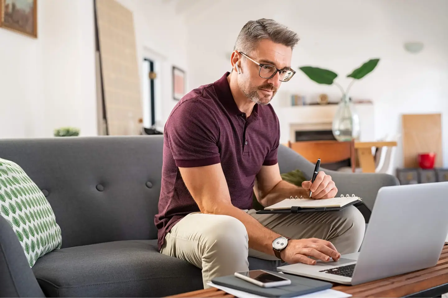 Man on couch using laptop and taking notes