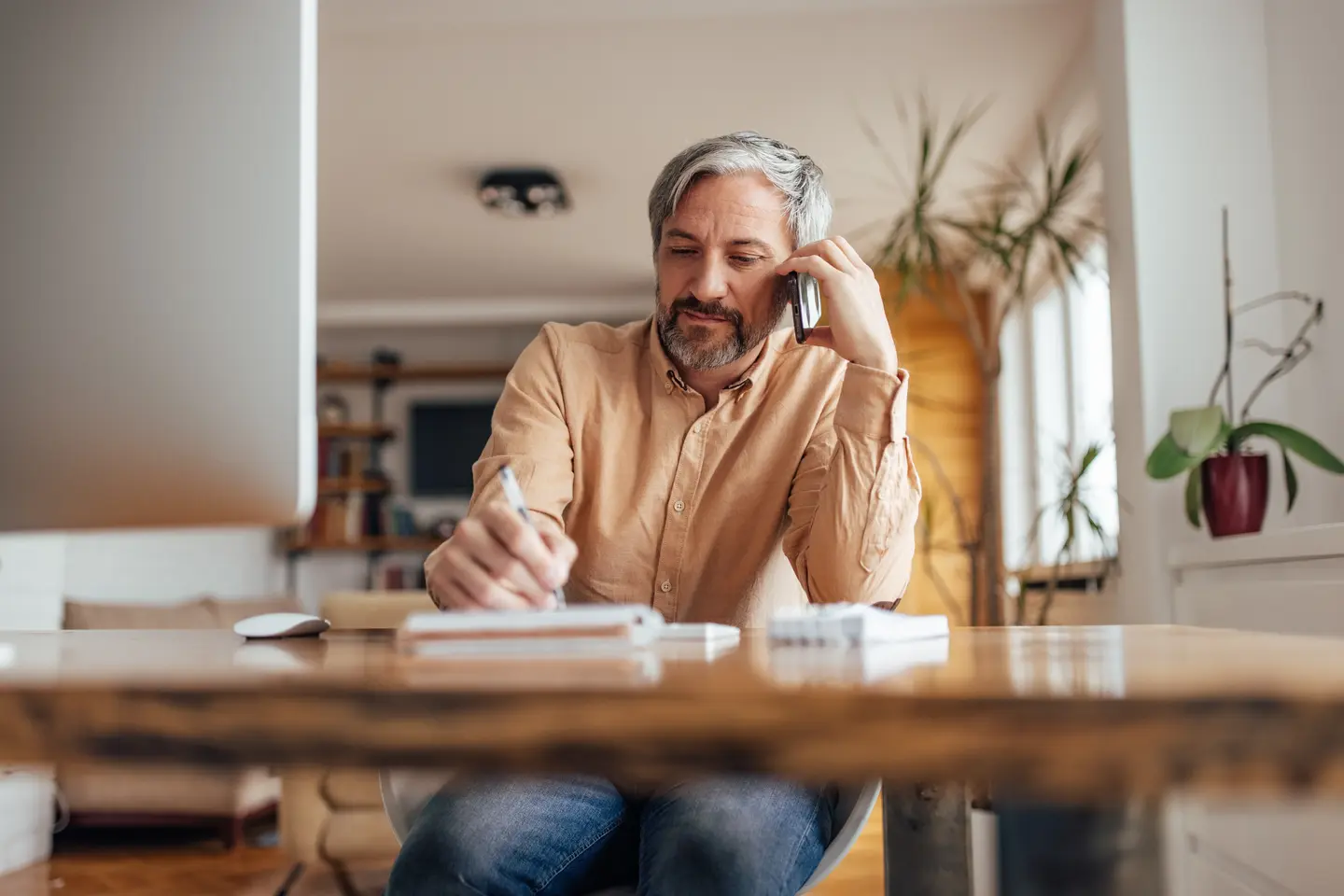 Man on phone call, taking notes at home office
