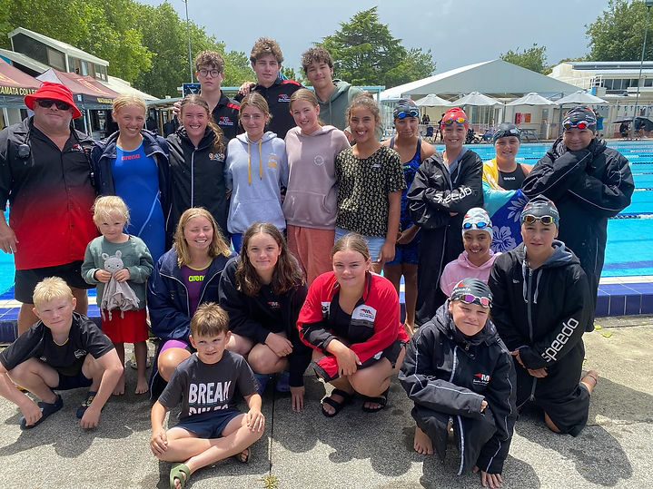 Group of swimmers, coaches, and children by a swimming pool, one child wears "BREAK".