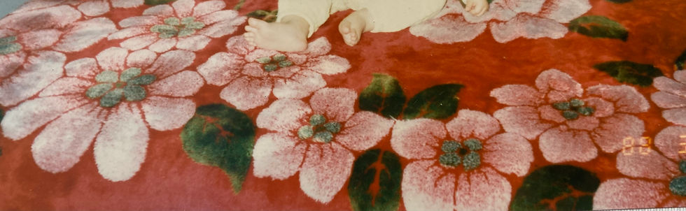 Baby feet on a red floral-patterned carpet with pink flowers and green leaves. Soft texture and warm colors create a cozy vibe.