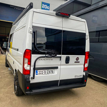 Rear view of a Fiat Ducato camper van showing the back doors with a bike rack mounted on the left door. The branding "rjhoward bespoke conversions" is visible on the lower right door.