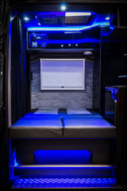 Inside, the bench seat is transformed into a flatbed, illuminated by soft blue LED lighting. The cozy sleeping area is tucked under a closed window shade, ensuring privacy and comfort.