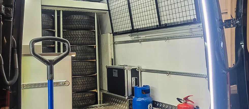Rear view of the SC Rally Sprinter's workshop with the doors open and the full lighting system illuminated. A bright LED perimeter, ceiling lighting and work lights create excellent visibility, while the tyre rack, load rails, protective flooring and open working space demonstrate the practical thinking behind the conversion.