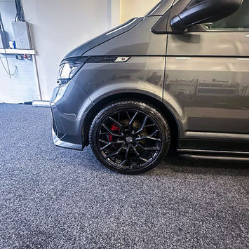 Close-up of the front wheel area on a grey Volkswagen camper van, showing a black multi-spoke alloy wheel, low-profile tyre, and red brake caliper. The image emphasizes the van’s upgraded performance-inspired styling and detailed exterior finish.