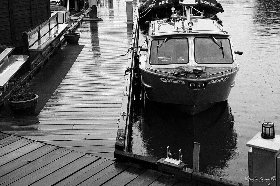 Boat docked on a rainy day, beside a wooden pier. Reflections in water, moody black-and-white scene. Nanaimo.